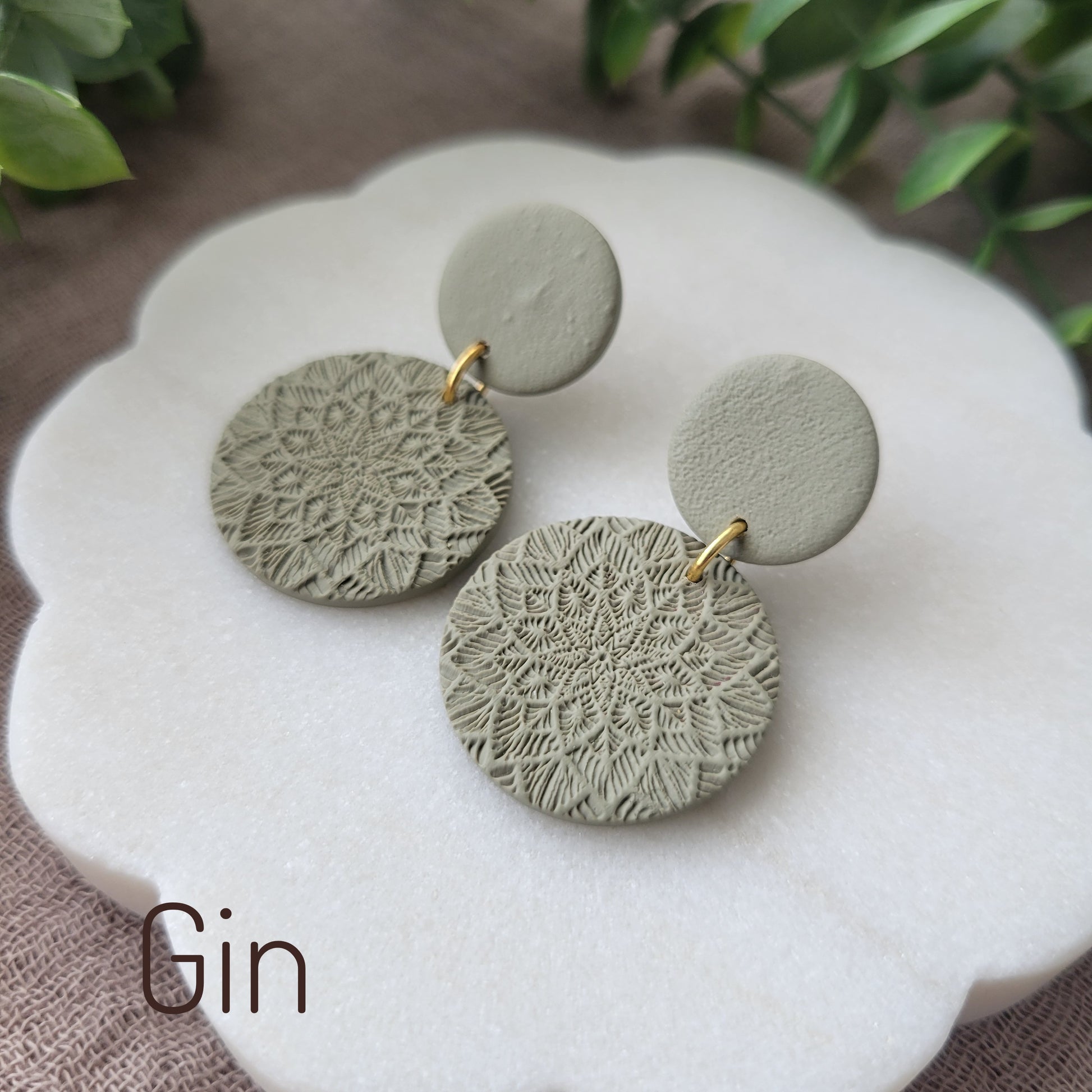 Side view of a pair of green mandala textured earrings displayed on a white round scalloped tray.