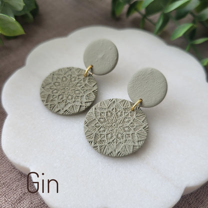Side view of a pair of green mandala textured earrings displayed on a white round scalloped tray.