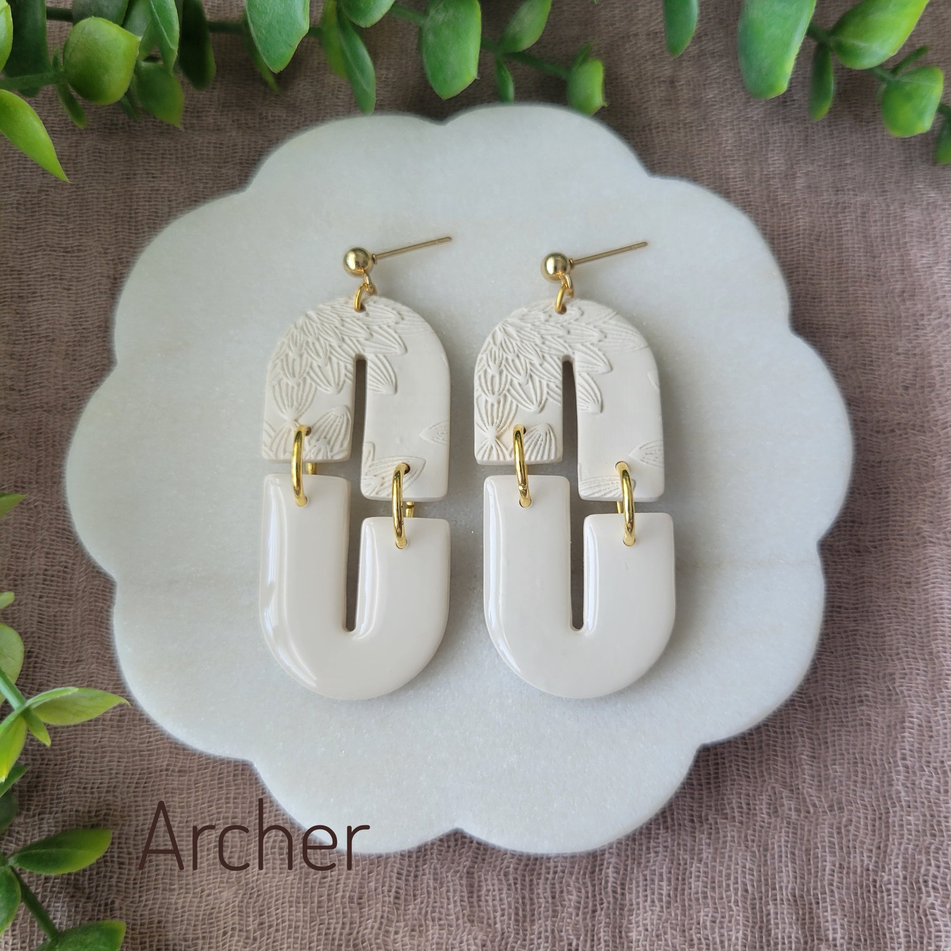 Top view of a pair of cream earrings with bloom texture displayed on a white round scalloped tray.