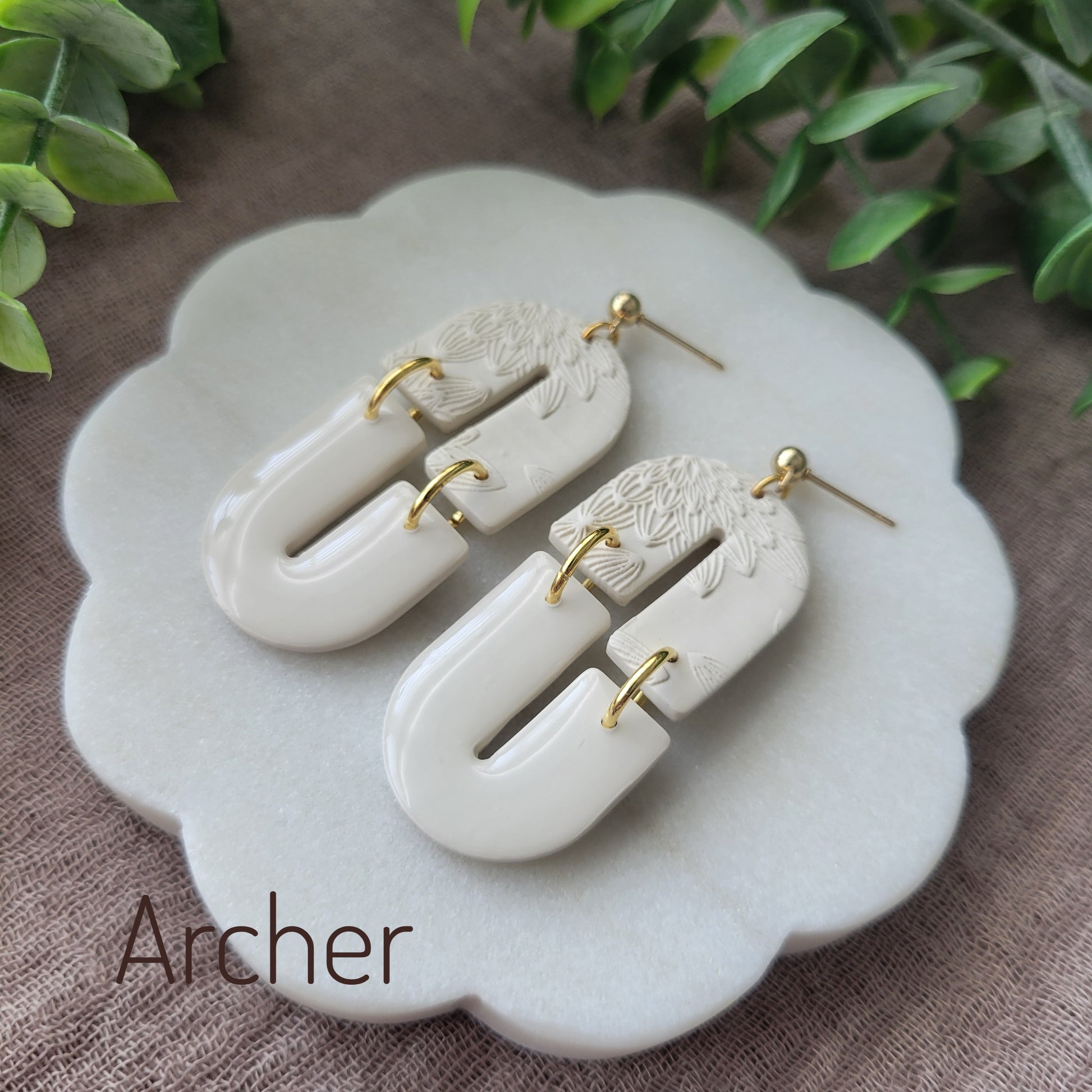Side view of a pair of cream earrings with bloom texture displayed on a white round scalloped tray.