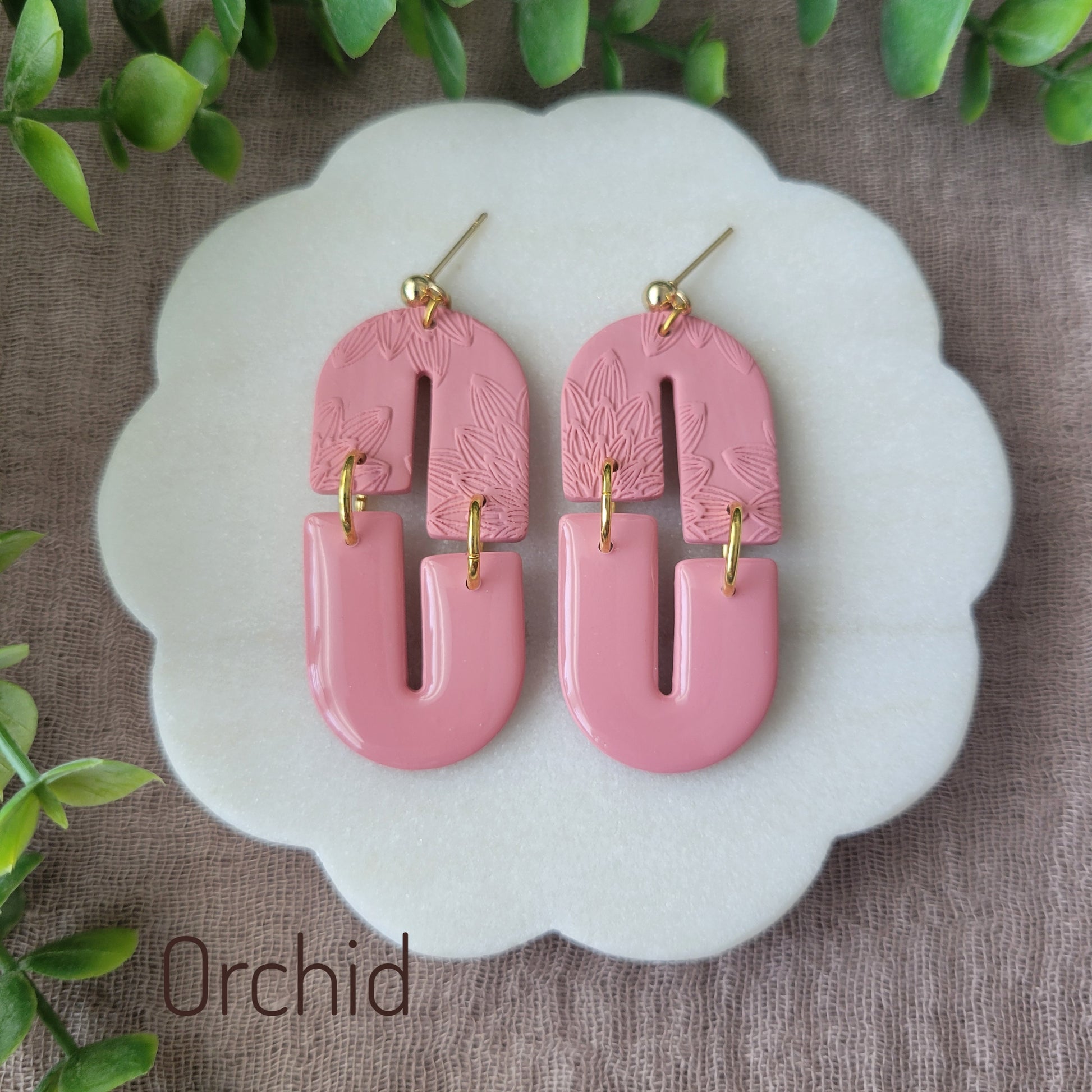 Top view of a pair of pink earrings with bloom texture displayed on a white round scalloped tray.