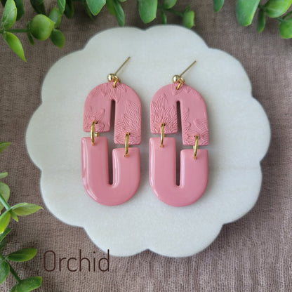 Top view of a pair of pink earrings with bloom texture displayed on a white round scalloped tray.