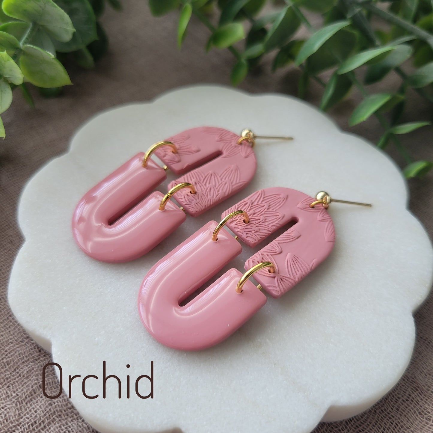 Side view of a pair of pink earrings with bloom texture displayed on a white round scalloped tray.