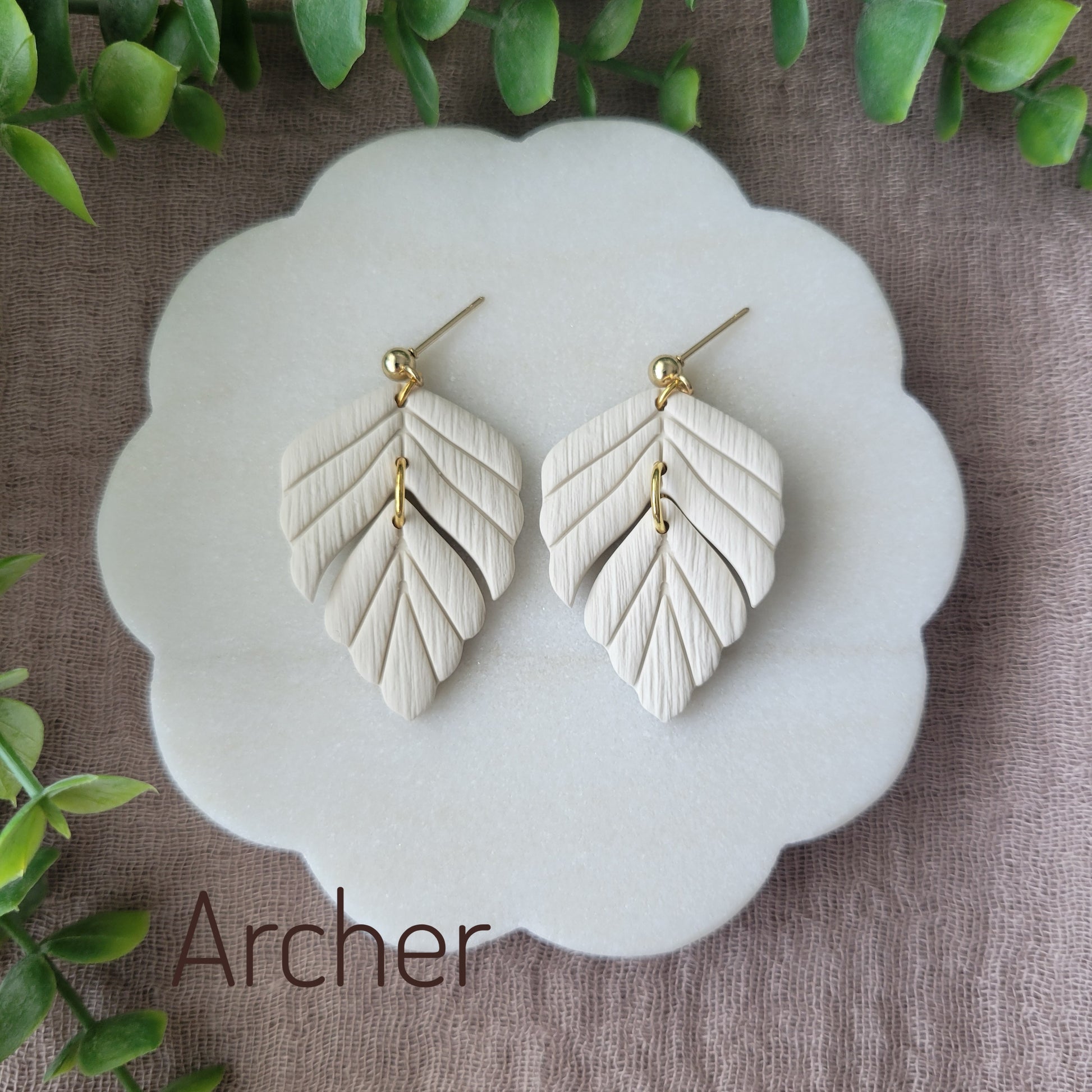 Top view of a pair of cream leaf shaped earrings displayed on a white scalloped tray.