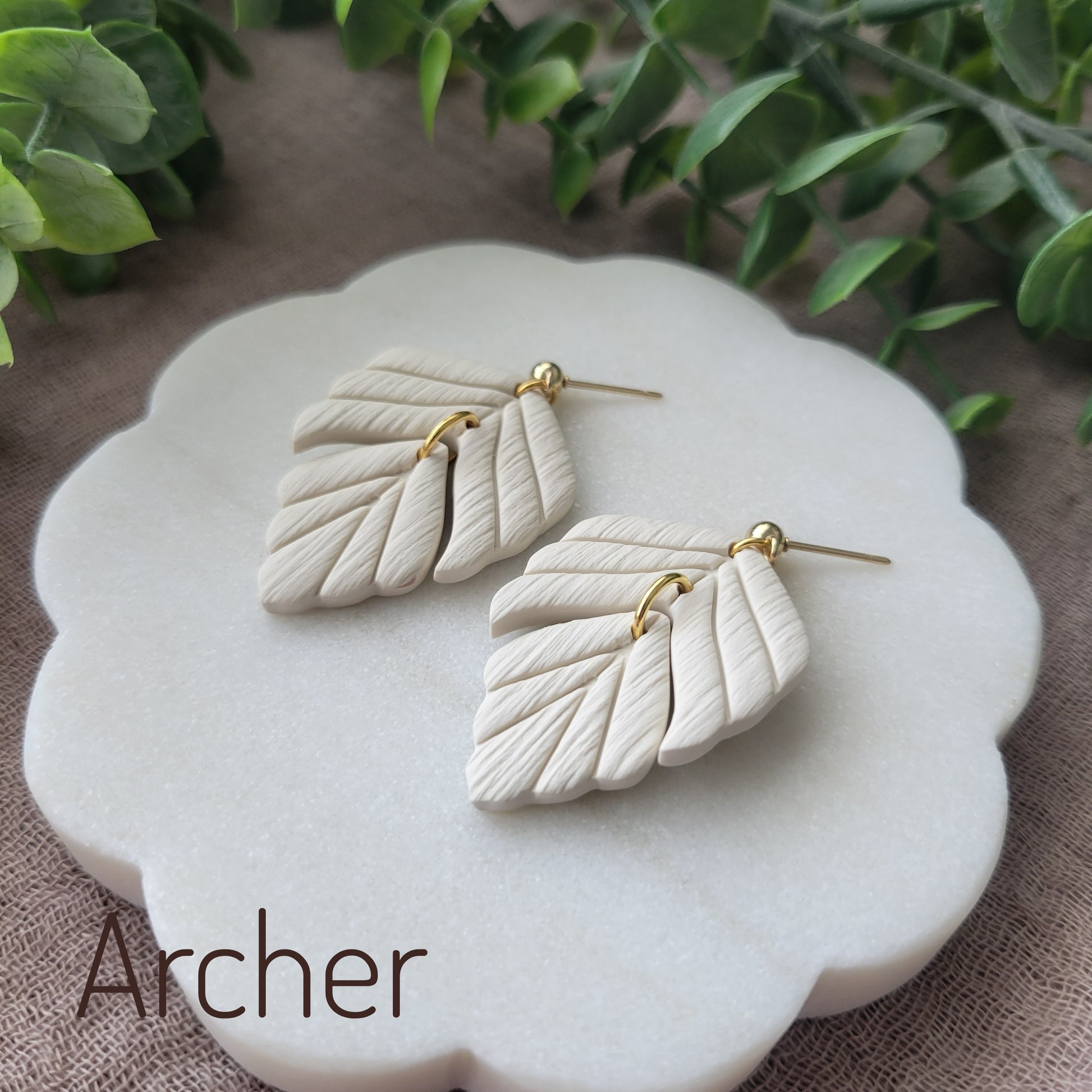 Side view of a pair of cream leaf shaped earrings displayed on a white scalloped tray.