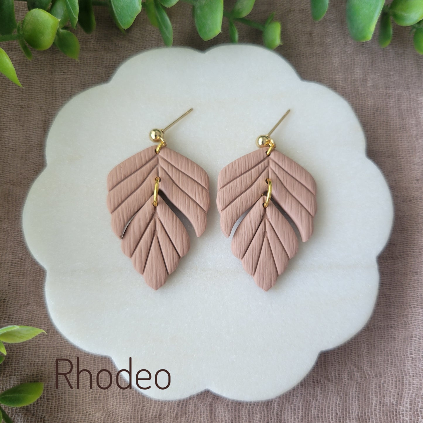 Top view of a pair of brown leaf shaped earrings displayed on a white scalloped tray.