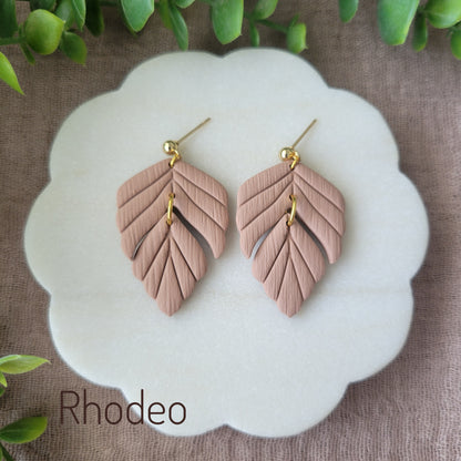 Top view of a pair of brown leaf shaped earrings displayed on a white scalloped tray.