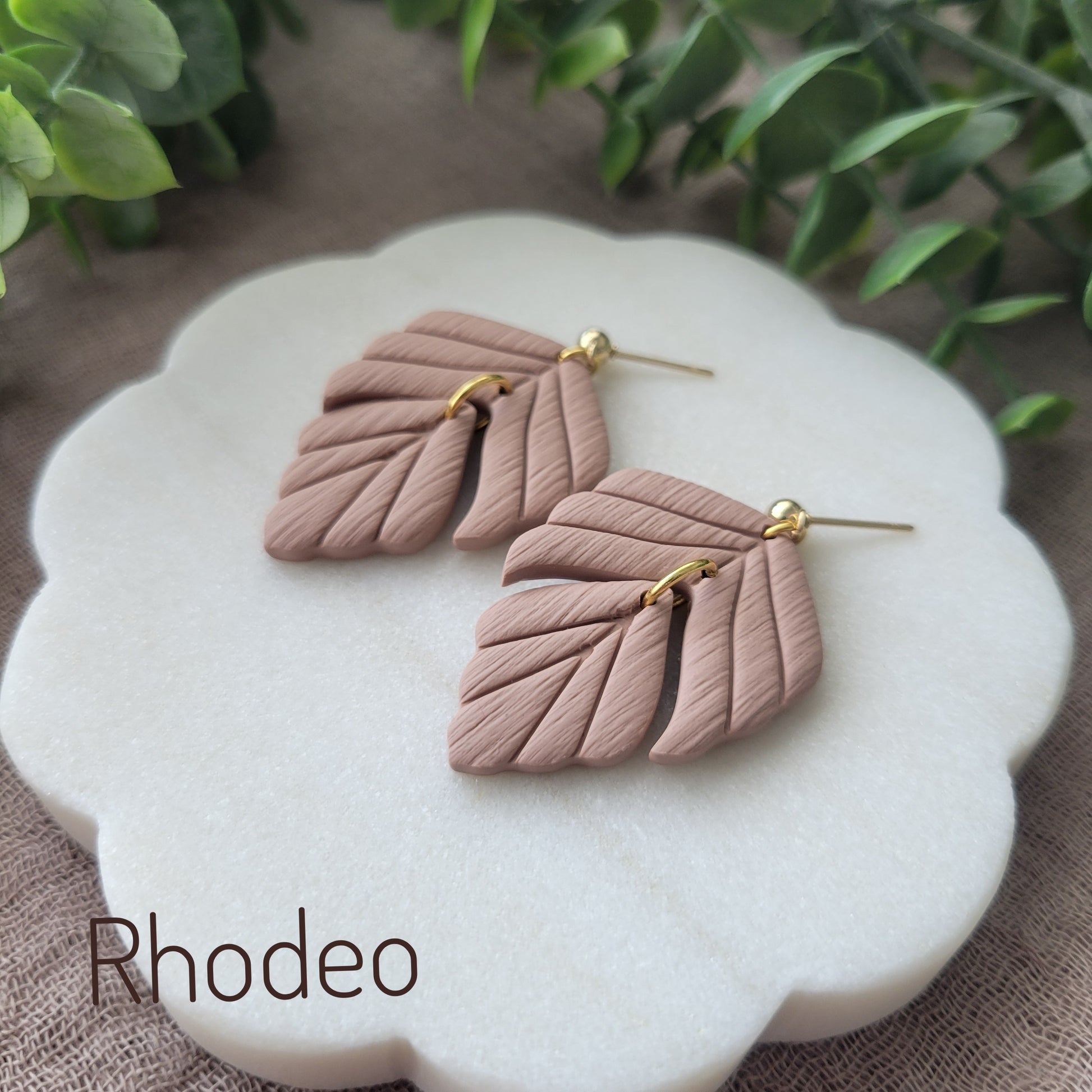 Side view of a pair of brown leaf shaped earrings displayed on a white scalloped tray.