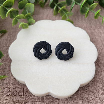 Top view of a pair of black knot stud earrings displayed on a white round scalloped tray.