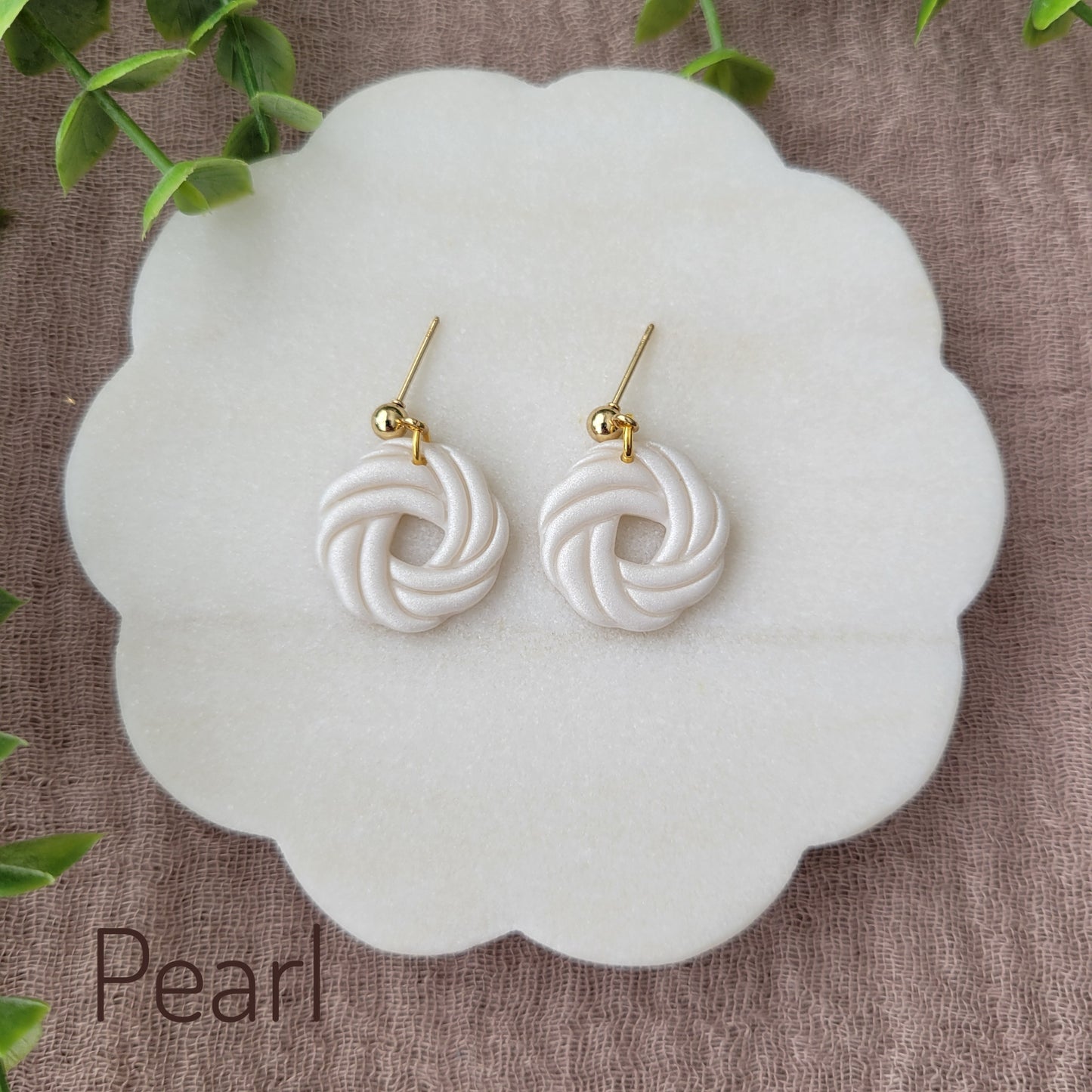 Top view of a pair of pearl knot dangle earrings displayed on a white round scalloped tray.