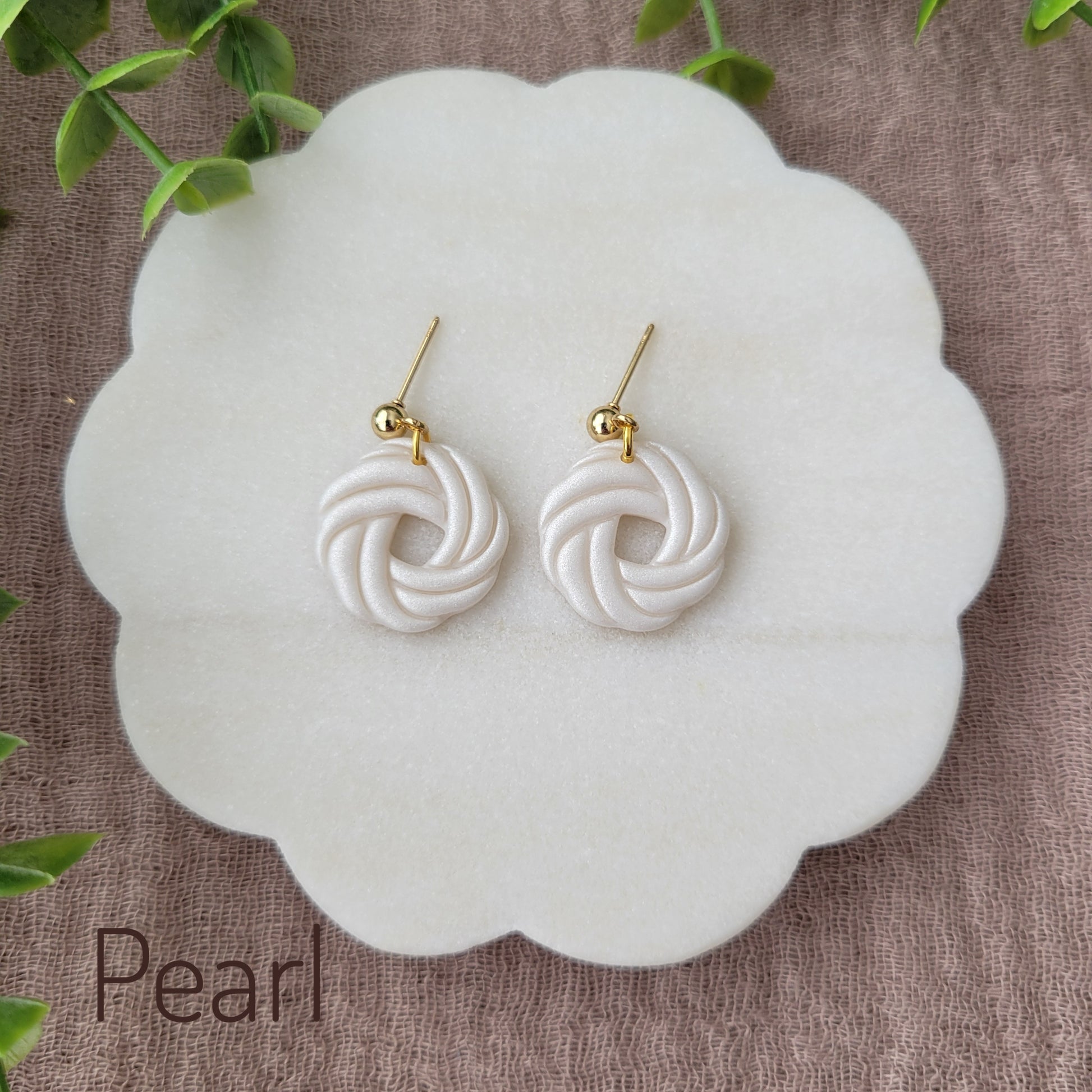 Top view of a pair of pearl knot dangle earrings displayed on a white round scalloped tray.