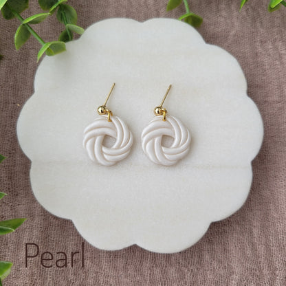 Top view of a pair of pearl knot dangle earrings displayed on a white round scalloped tray.