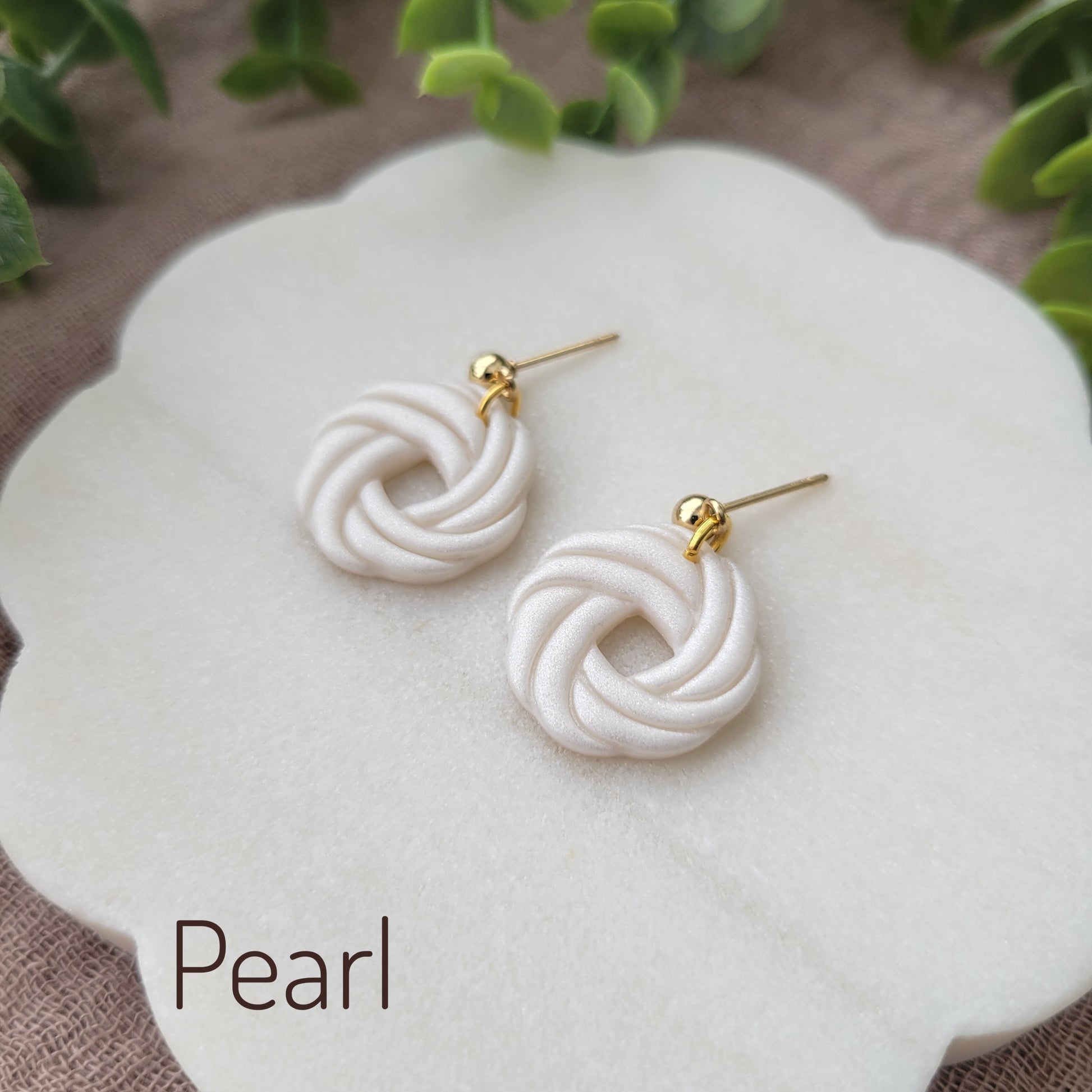 Side view of a pair of pearl knot dangle earrings displayed on a white round scalloped tray.
