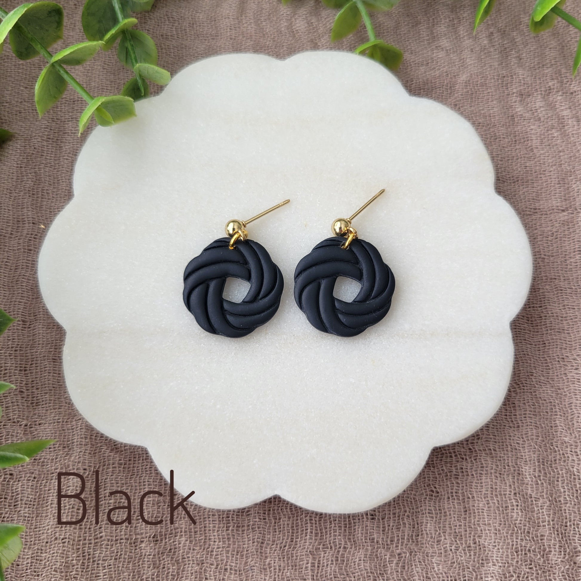 Top view of a pair of black knot dangle earrings displayed on a white round scalloped tray.