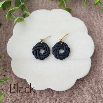 Top view of a pair of black knot dangle earrings displayed on a white round scalloped tray.