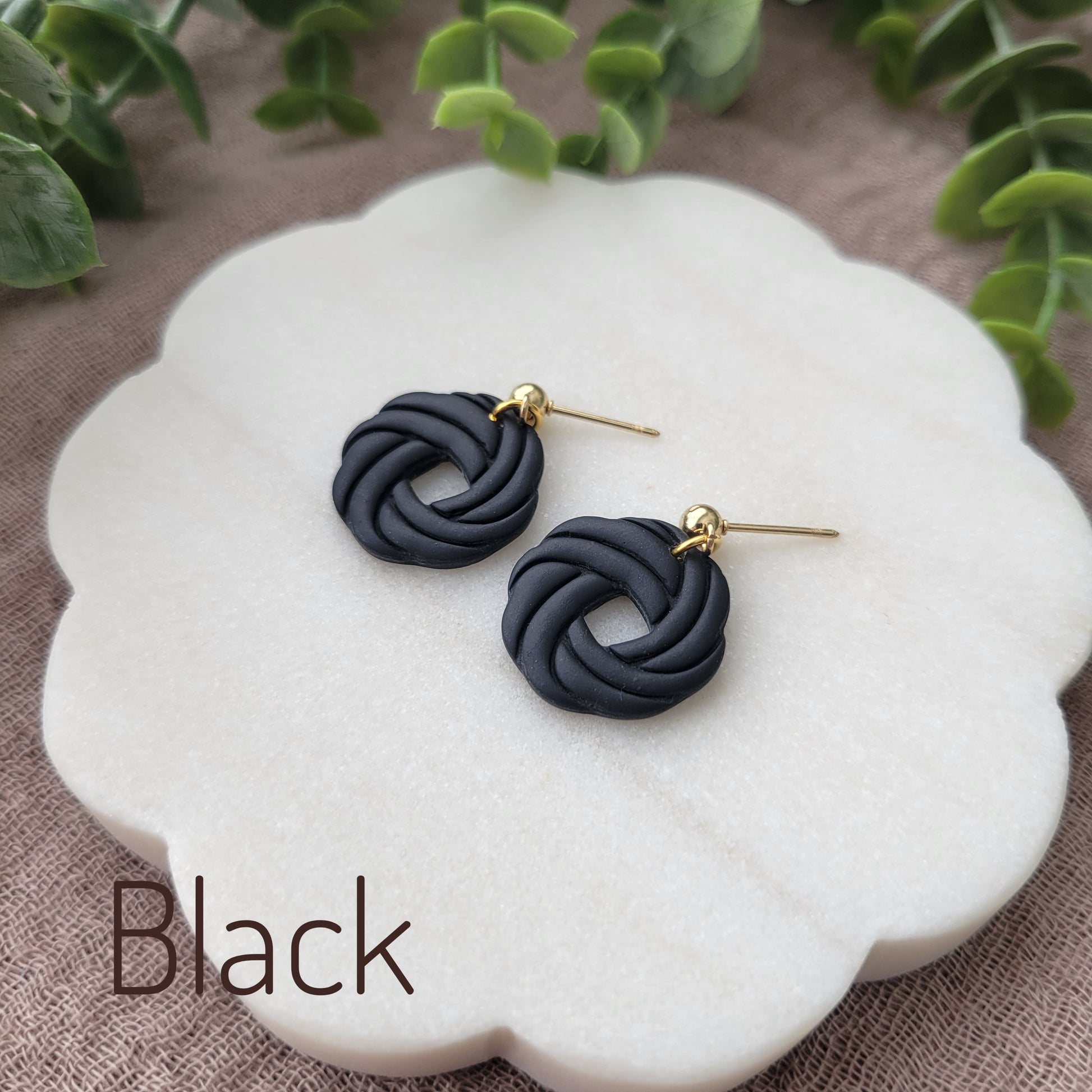 Side view of a pair of black knot dangle earrings displayed on a white round scalloped tray.