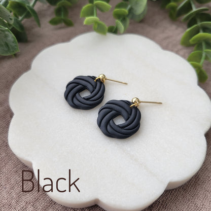 Side view of a pair of black knot dangle earrings displayed on a white round scalloped tray.