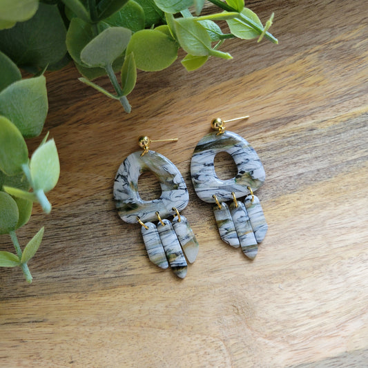 Top view of a pair of green, white, black, brown marbled earrings displayed on a wooden tray.