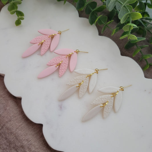 Side view of two pairs of leaf drop shaped earrings with a scalloped mandala texture displayed on a white scalloped tray.