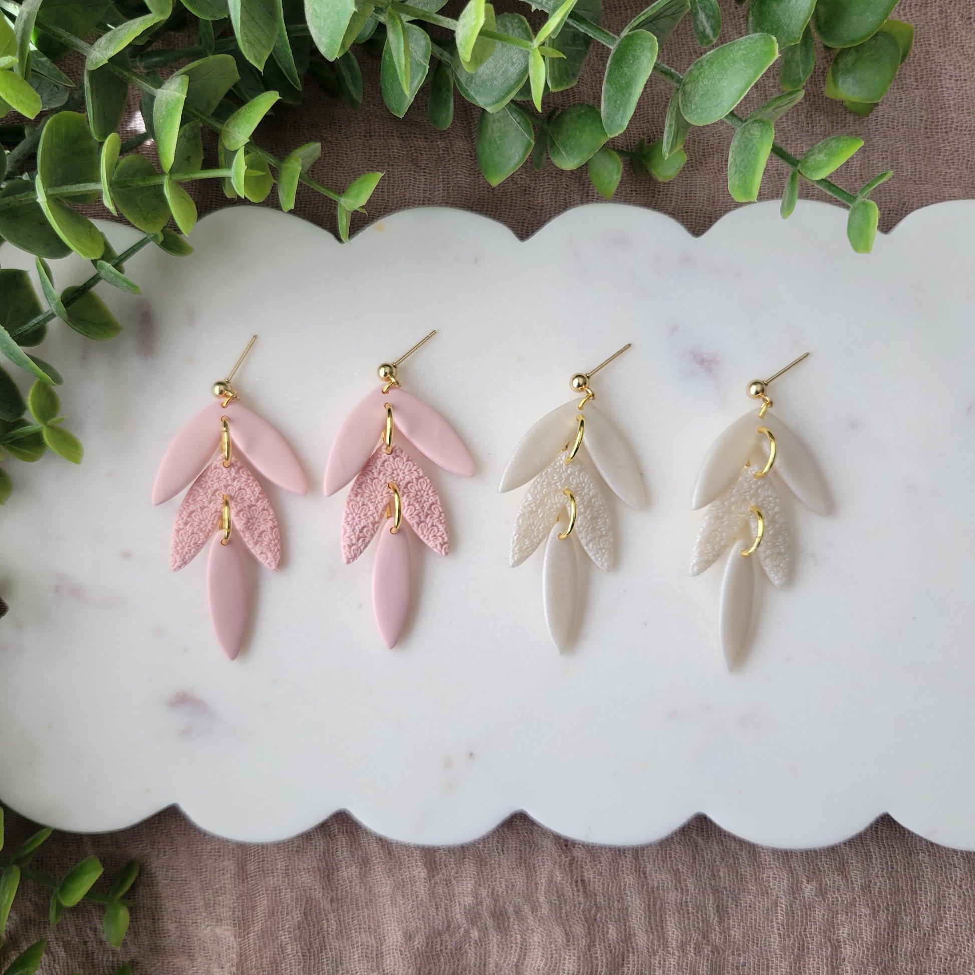 Top view of two pairs of leaf drop shaped earrings with a scalloped mandala texture displayed on a white scalloped tray.