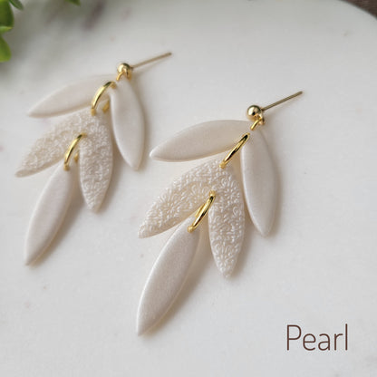 Close up side view of a pair of pearl leaf drop shaped earrings with a scalloped mandala texture displayed on a white scalloped tray.