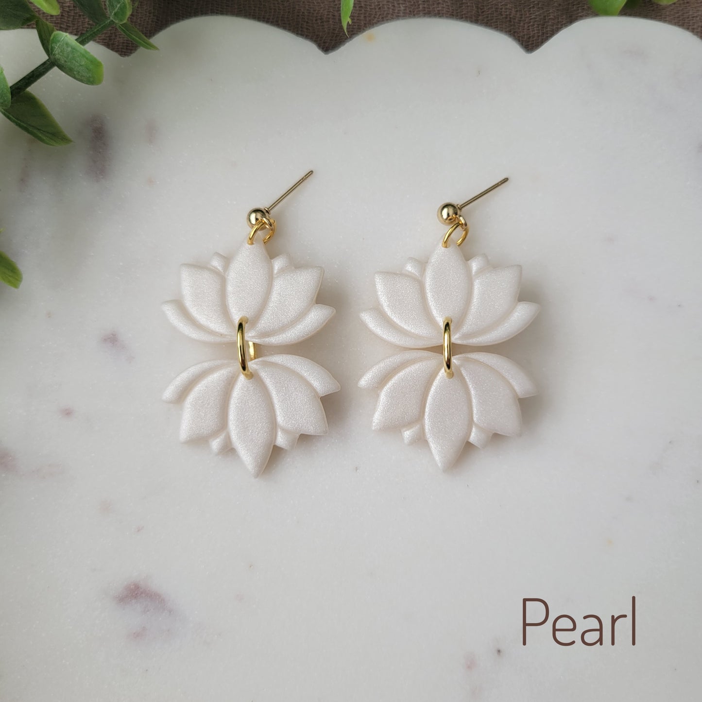 Top view of a pair of pearl lotus earrings displayed on a white round scalloped tray.