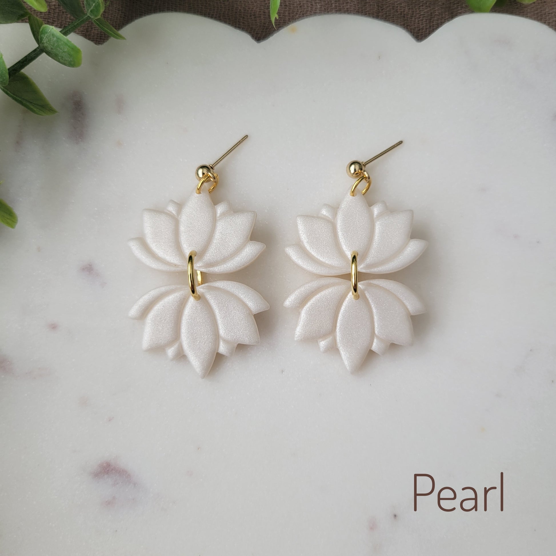 Top view of a pair of pearl lotus earrings displayed on a white round scalloped tray.