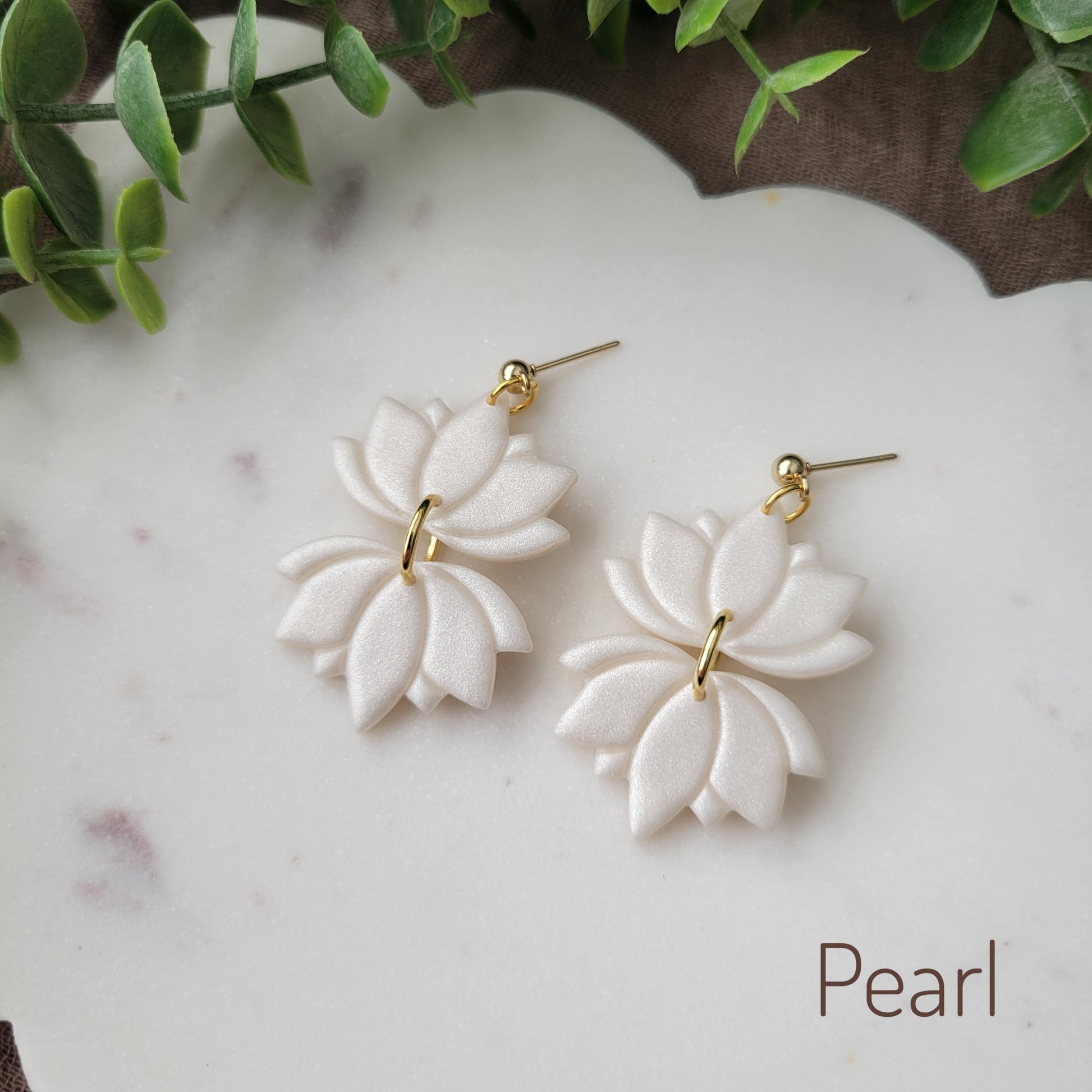 Side view of a pair of pearl lotus earrings displayed on a white round scalloped tray.