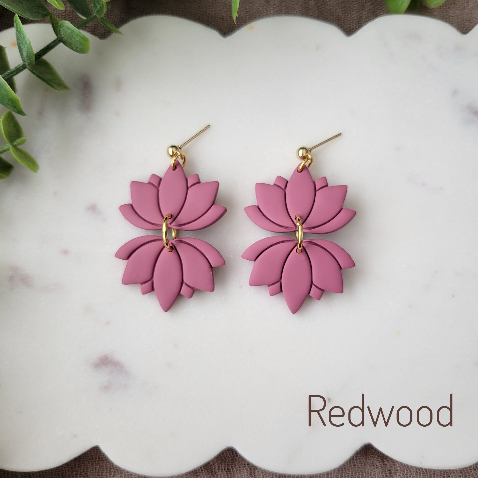 Top view of a pair of pink lotus earrings displayed on a white round scalloped tray.