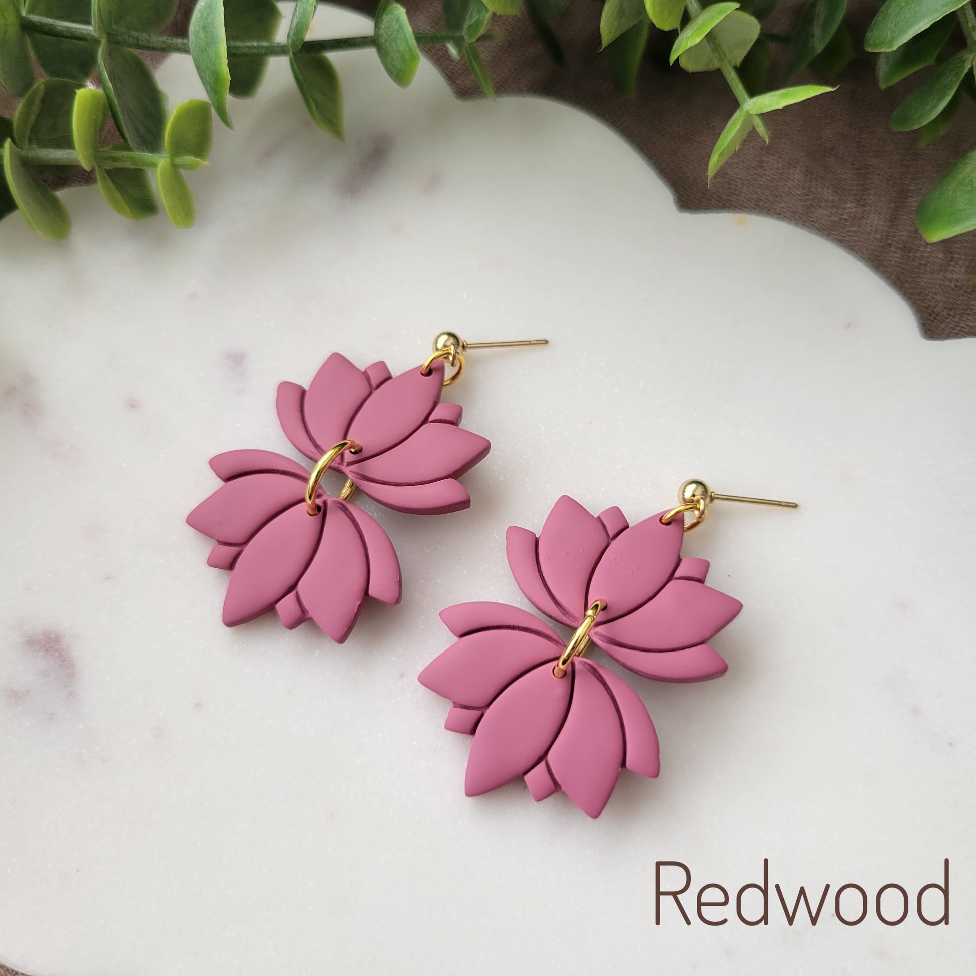 Side view of a pair of pink lotus earrings displayed on a white round scalloped tray.