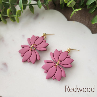 Side view of a pair of pink lotus earrings displayed on a white round scalloped tray.