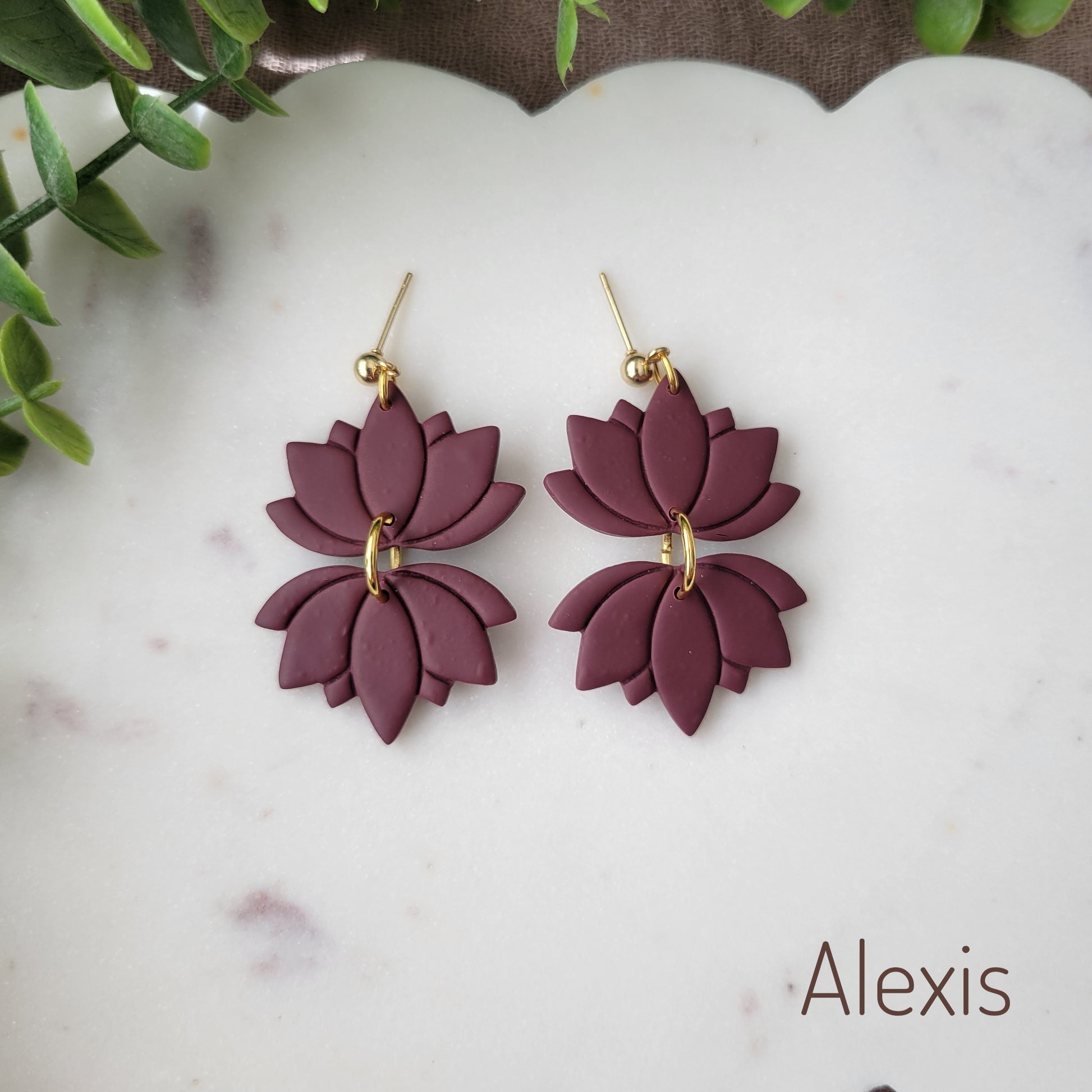 Top view of a pair of reddish purple lotus earrings displayed on a white round scalloped tray.