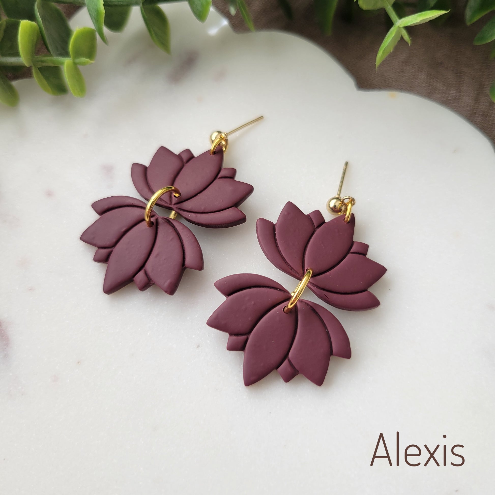 Side view of a pair of reddish purple lotus earrings displayed on a white round scalloped tray.