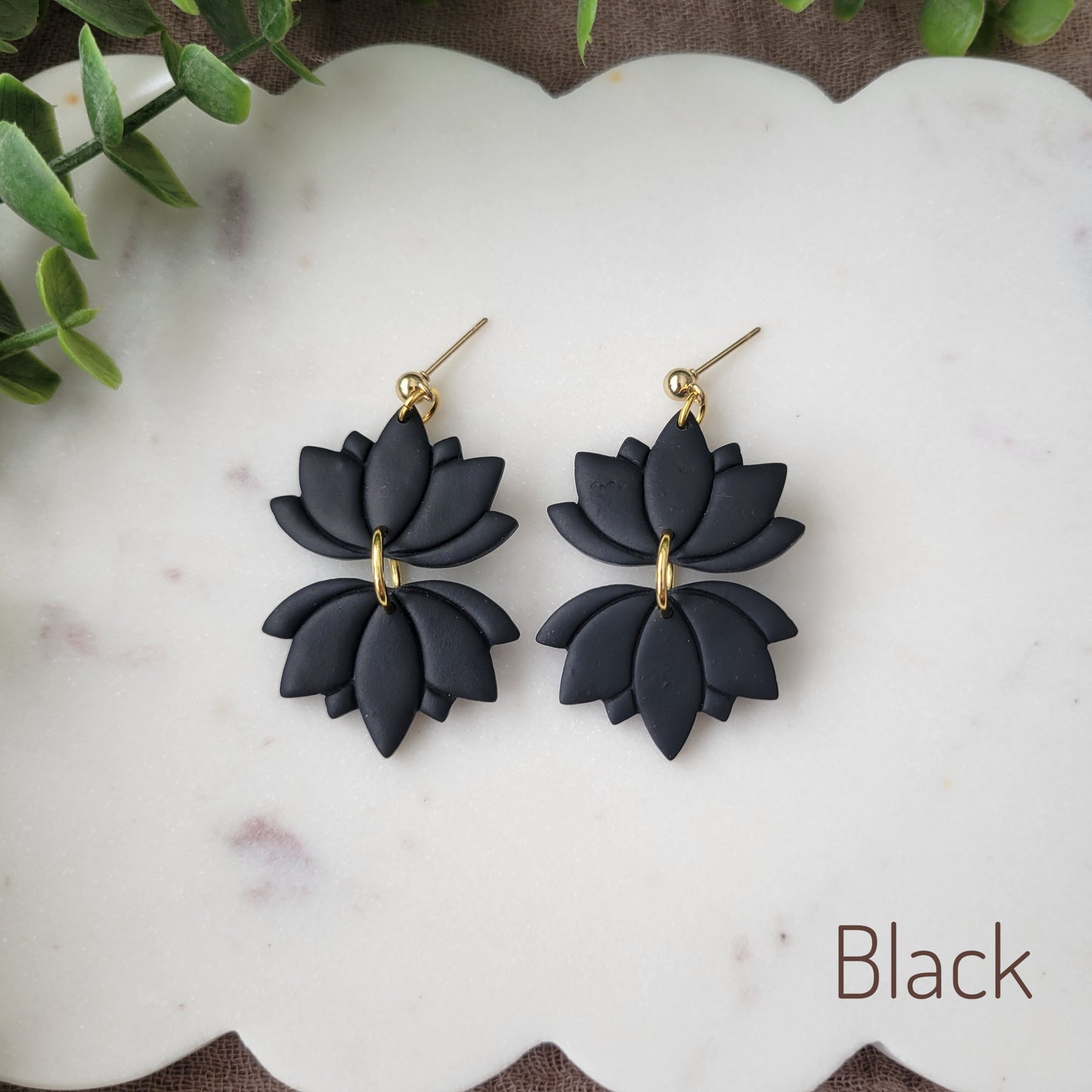 Top view of a pair of black lotus earrings displayed on a white round scalloped tray.