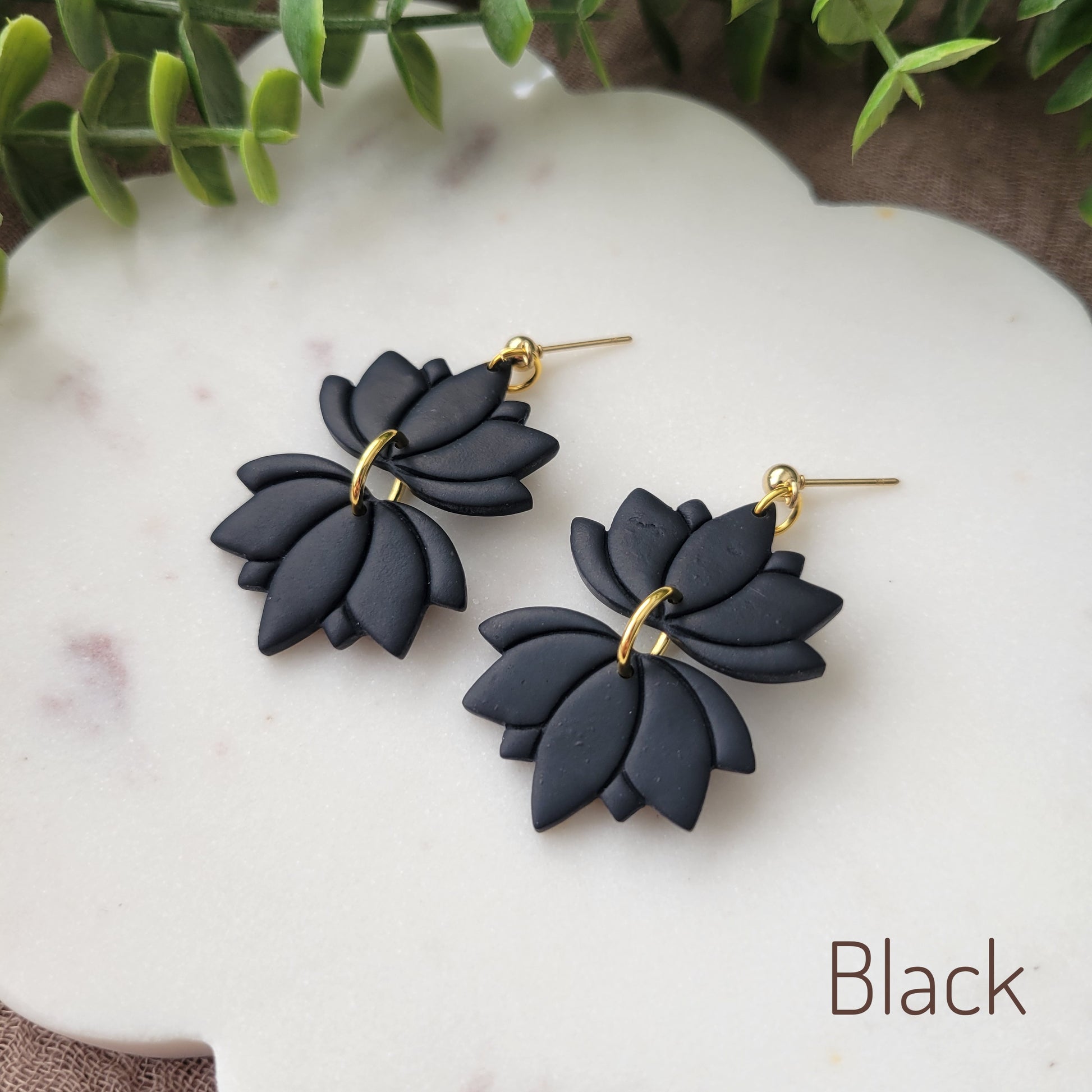 Side view of a pair of black lotus earrings displayed on a white round scalloped tray.
