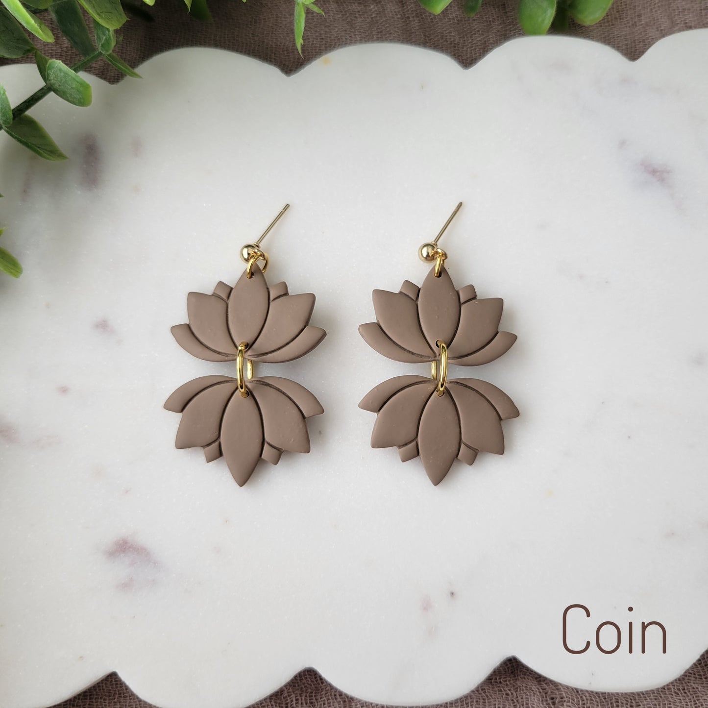 Top view of a pair of brown lotus earrings displayed on a white round scalloped tray.