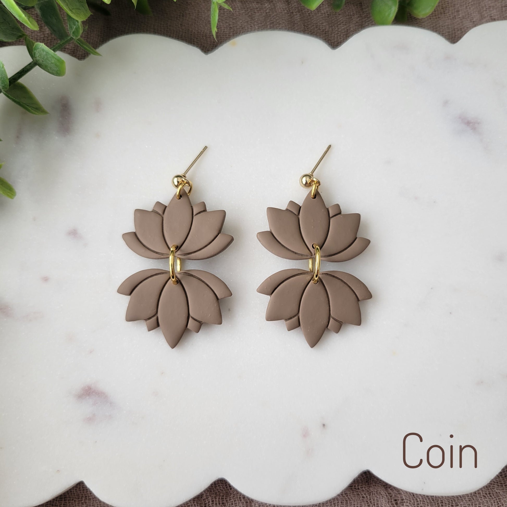 Top view of a pair of brown lotus earrings displayed on a white round scalloped tray.