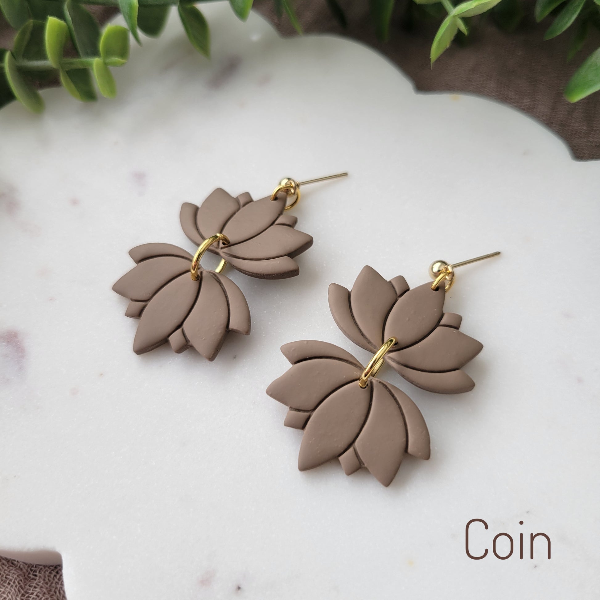 Side view of a pair of brown lotus earrings displayed on a white round scalloped tray.