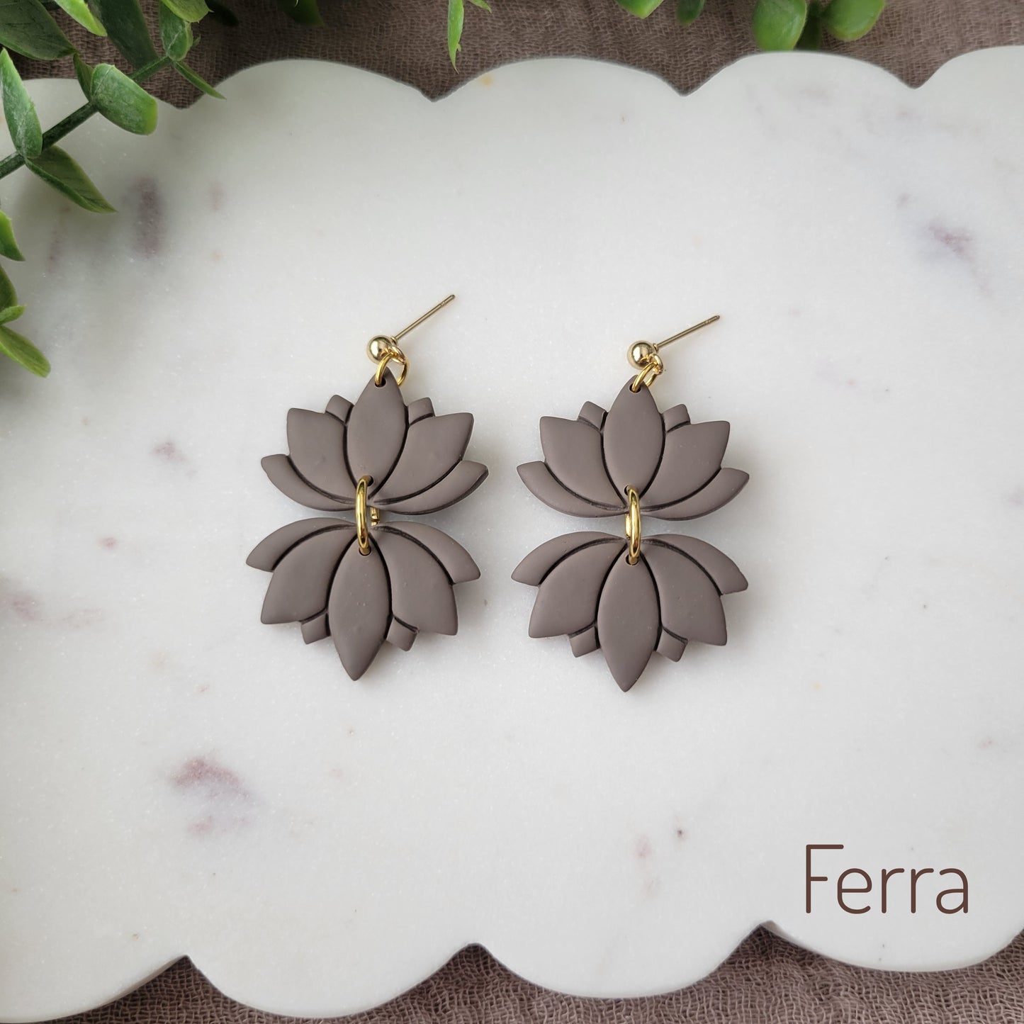 Top view of a pair of grayish brown lotus earrings displayed on a white round scalloped tray.