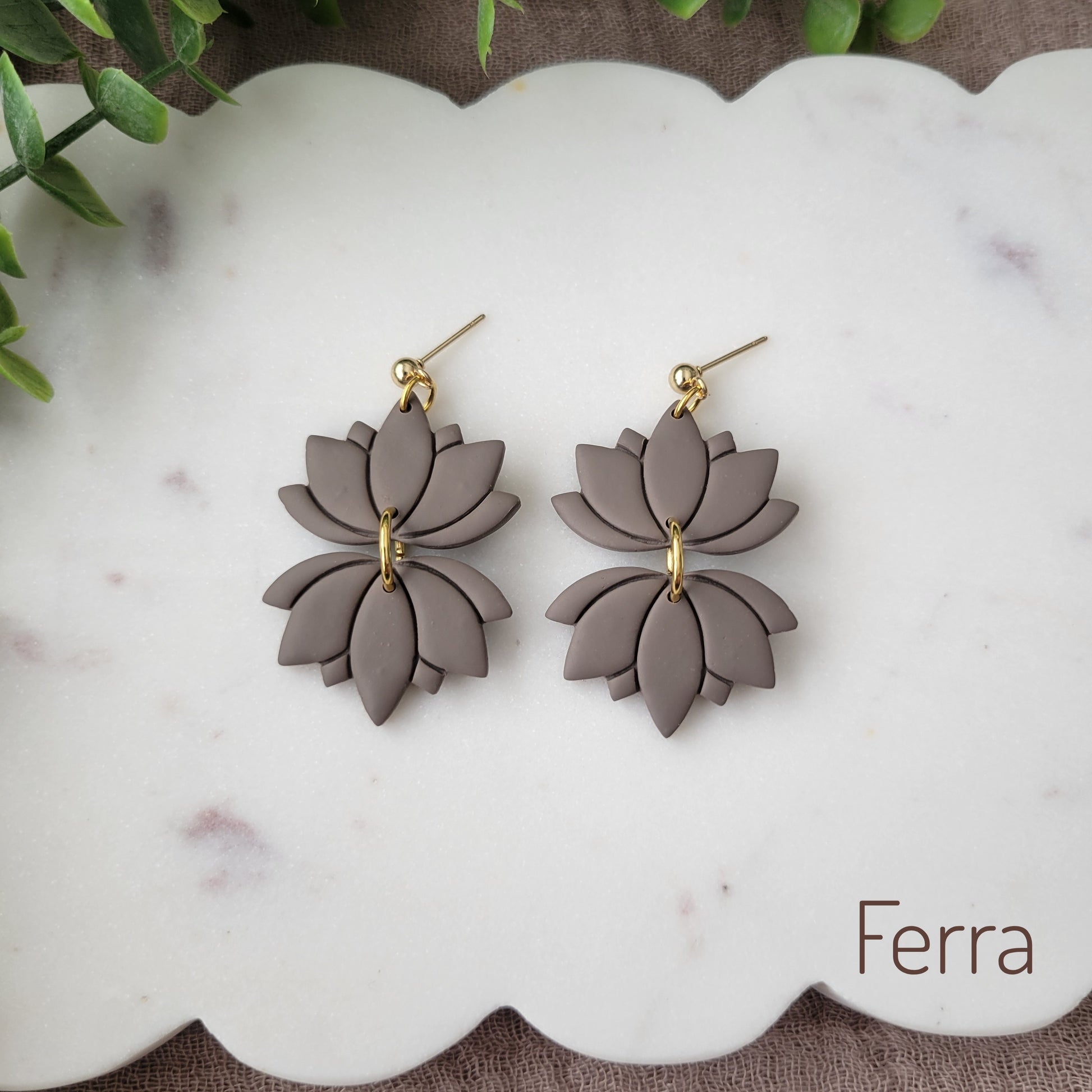 Top view of a pair of grayish brown lotus earrings displayed on a white round scalloped tray.