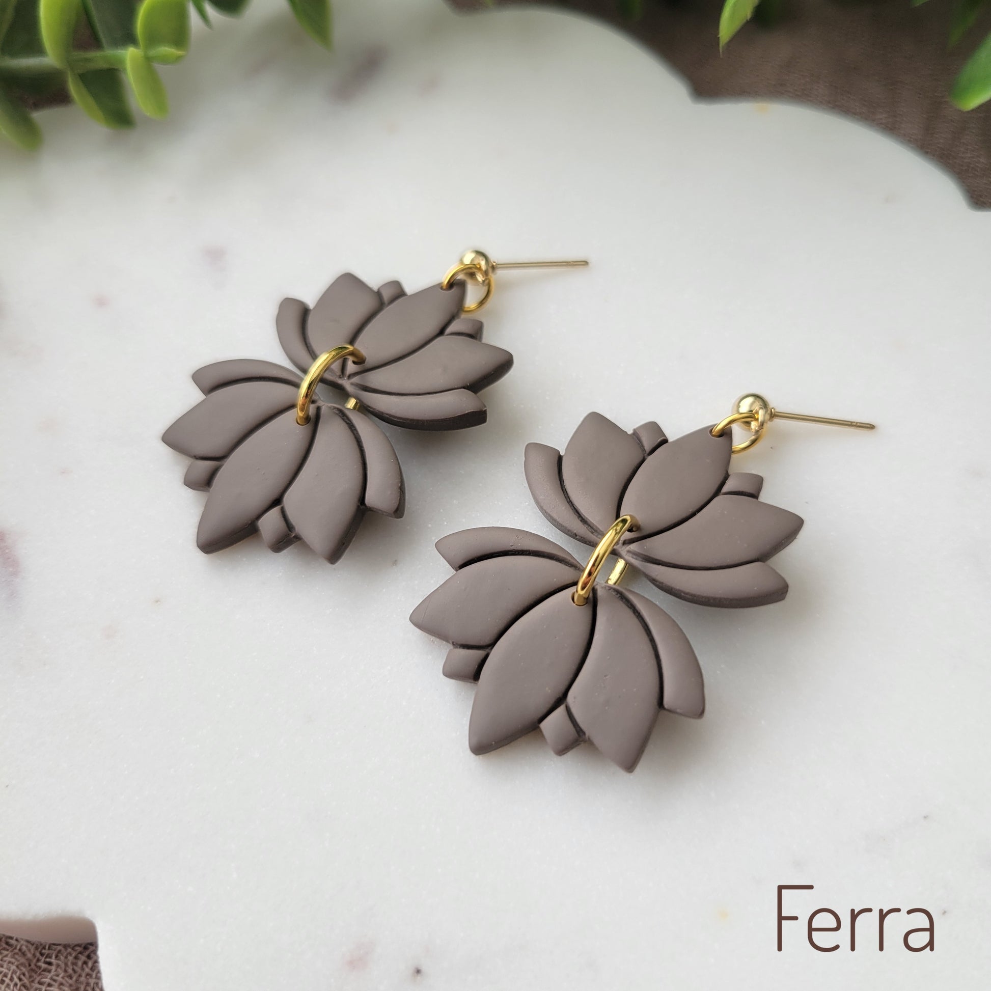 Side view of a pair of grayish brown lotus earrings displayed on a white round scalloped tray.