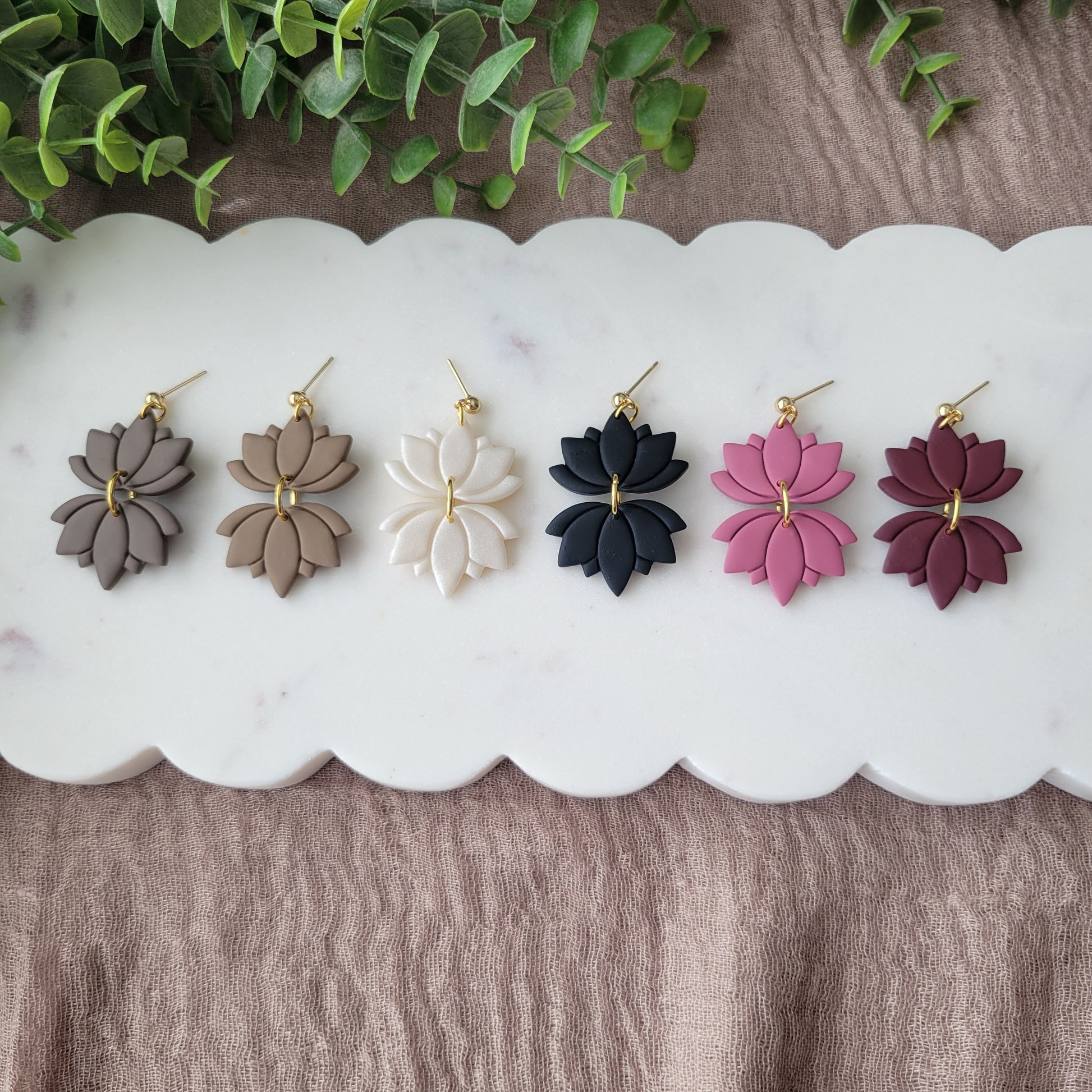 Top view of six lotus shaped earrings displayed on a white scalloped tray.