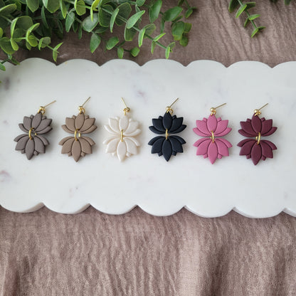 Top view of six lotus shaped earrings displayed on a white scalloped tray.