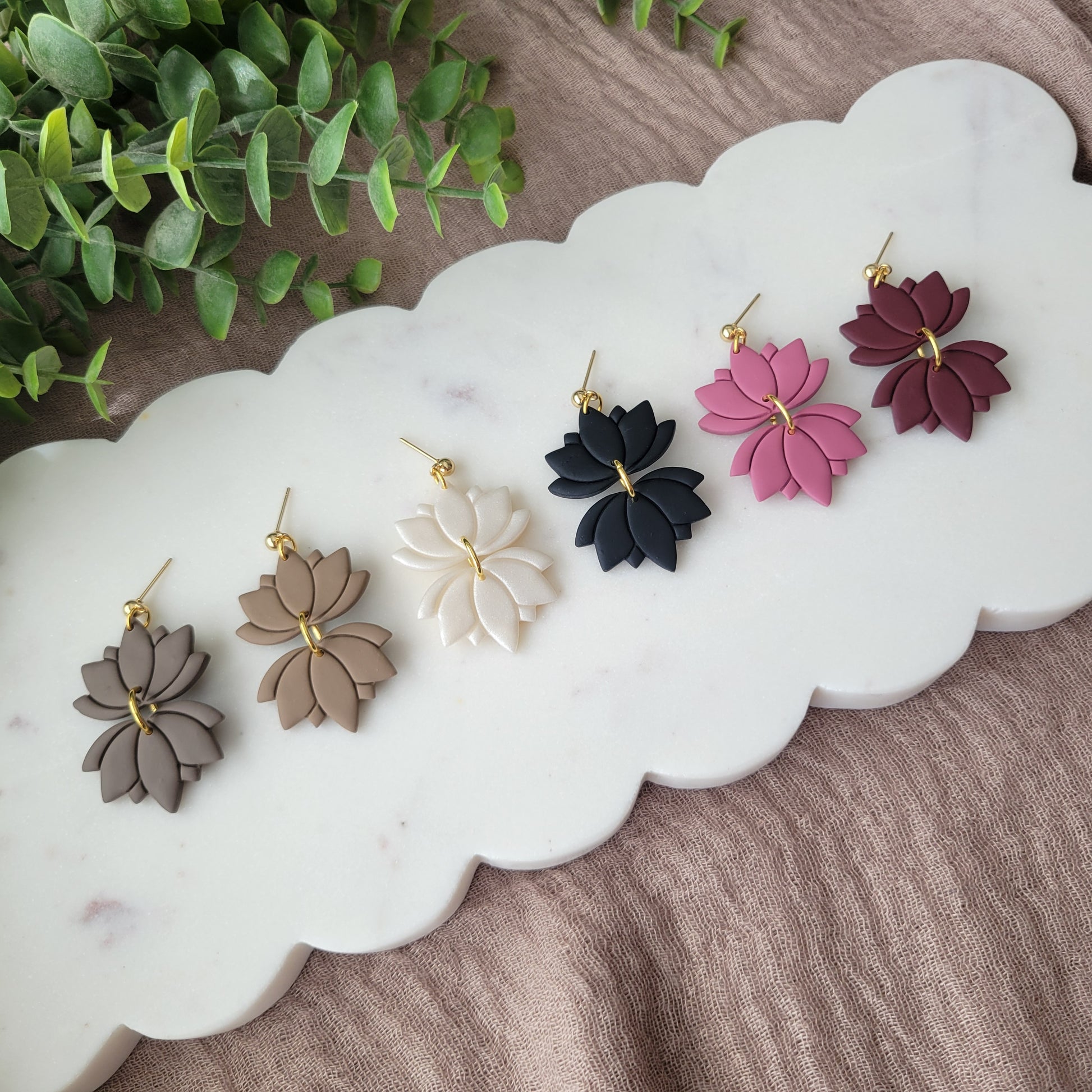 Left view of six lotus shaped earrings displayed on a white scalloped tray.