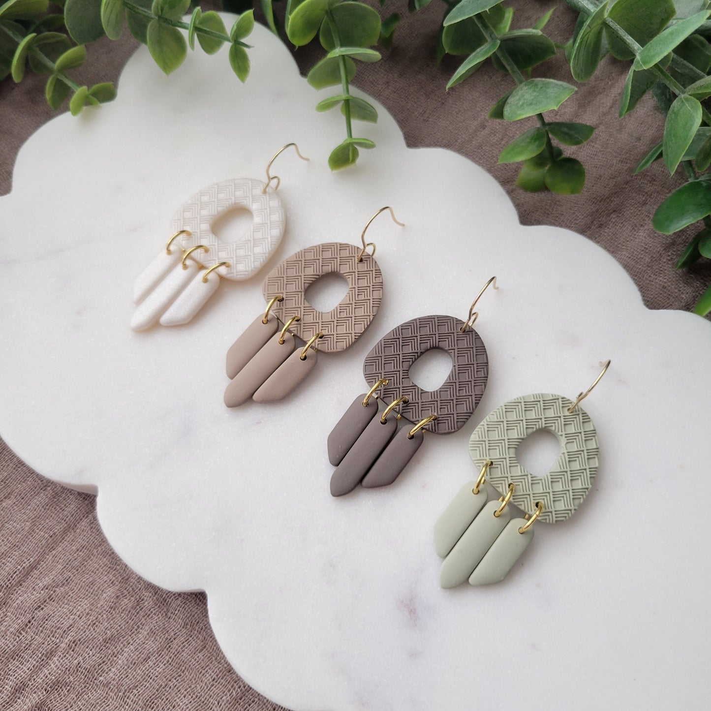 Side view of four earrings with lattice texture displayed on a white scalloped tray.