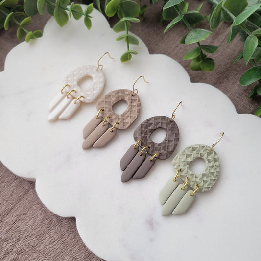 Side view of four earrings with lattice texture displayed on a white scalloped tray.