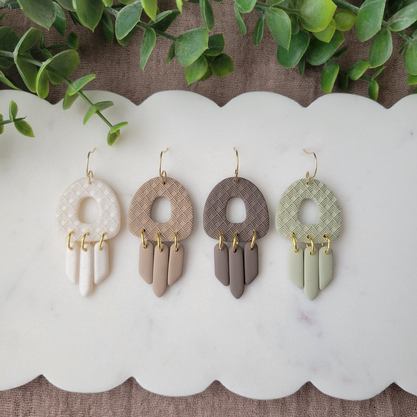 Top view of four earrings with lattice texture displayed on a white scalloped tray.