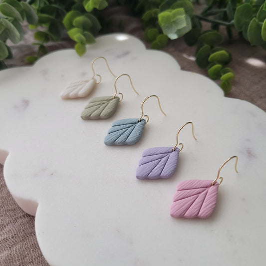 Right side view of five small leaf shaped earrings displayed on a white scalloped tray.