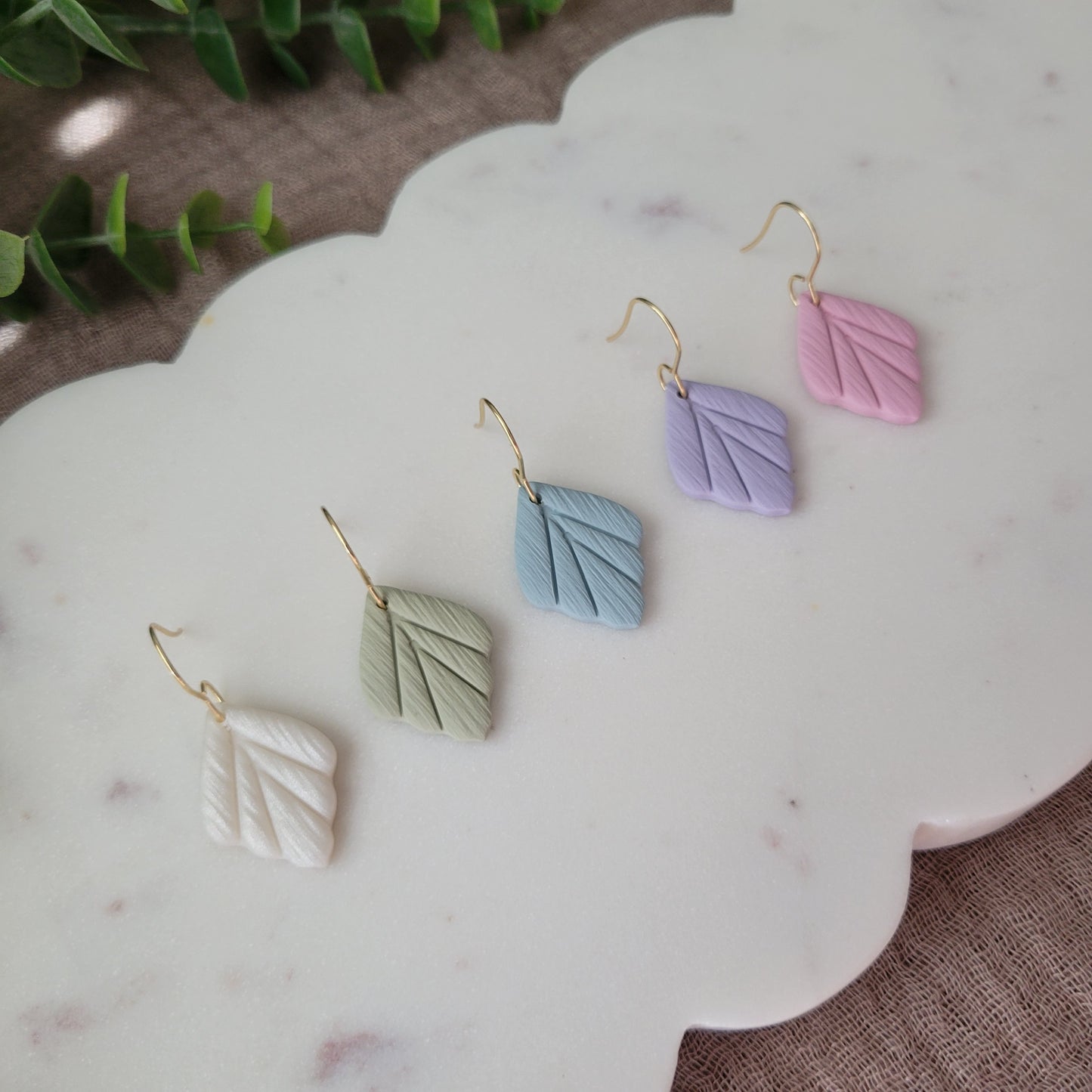 Left side view of five small leaf shaped earrings displayed on a white scalloped tray.