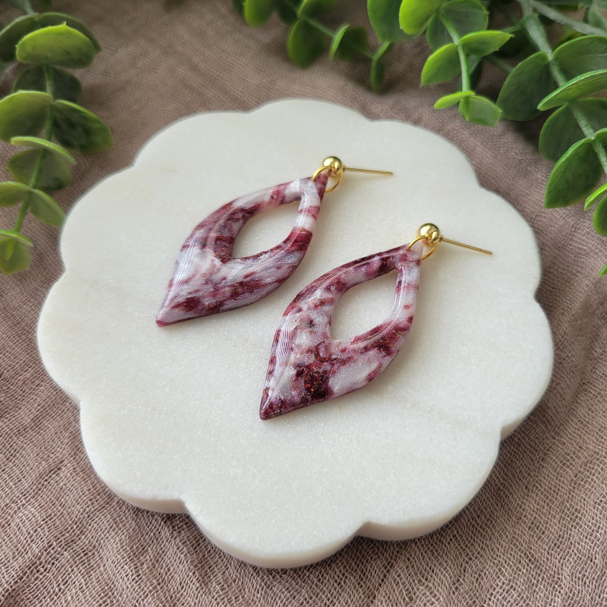 Right side view of a pair of maroon, pearl earrings displayed on a white round scalloped tray.